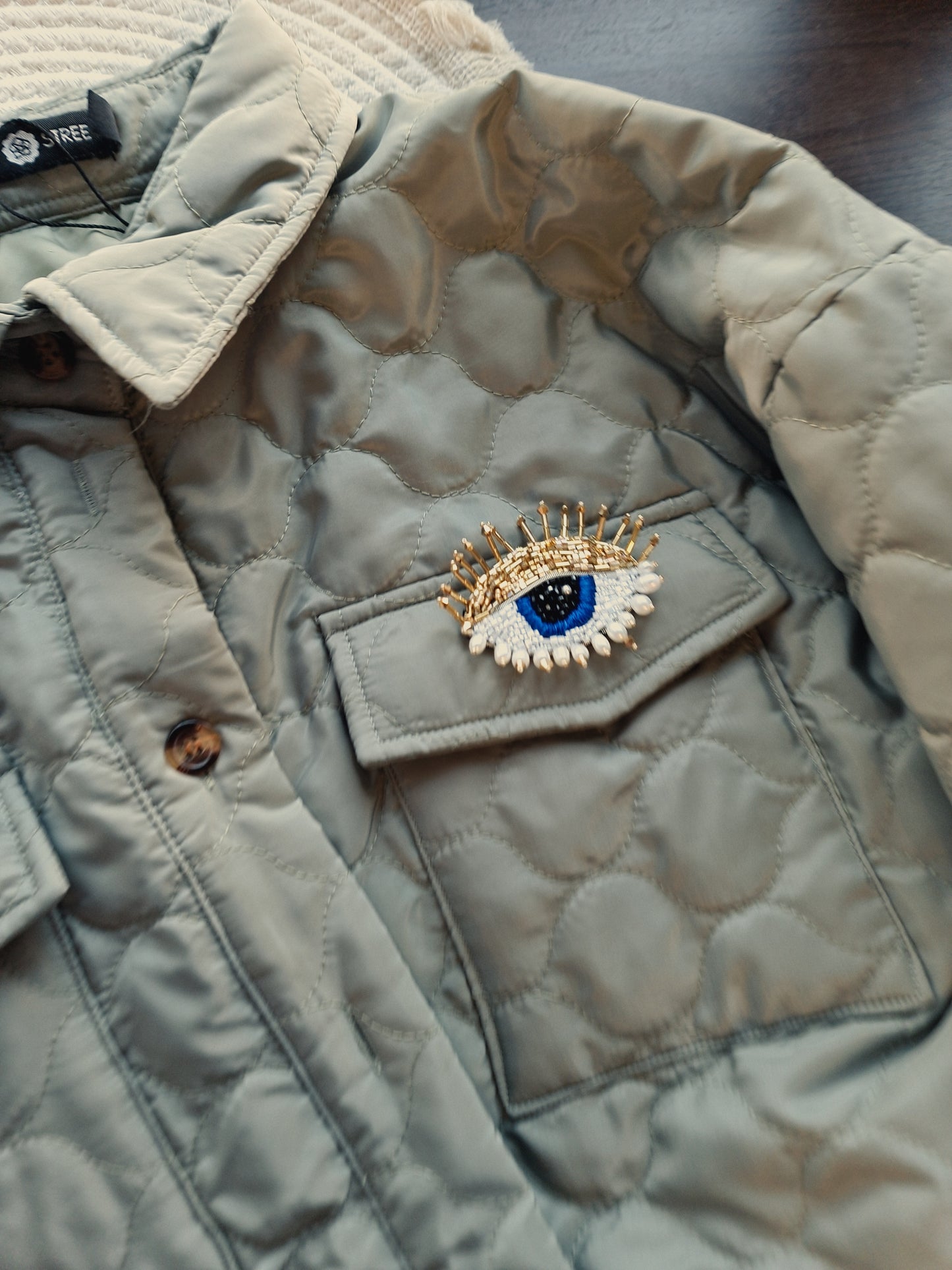 Close-up view of the intricate beadwork on the blue eye brooch, showcasing shimmering glass beads, crystals, and plastic beads fixed onto felt