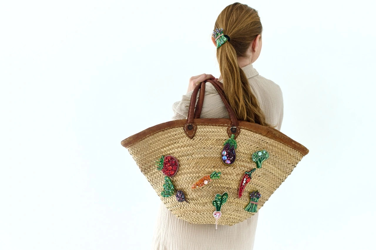 Person holding a woven bag with colorful embellishments on a white background