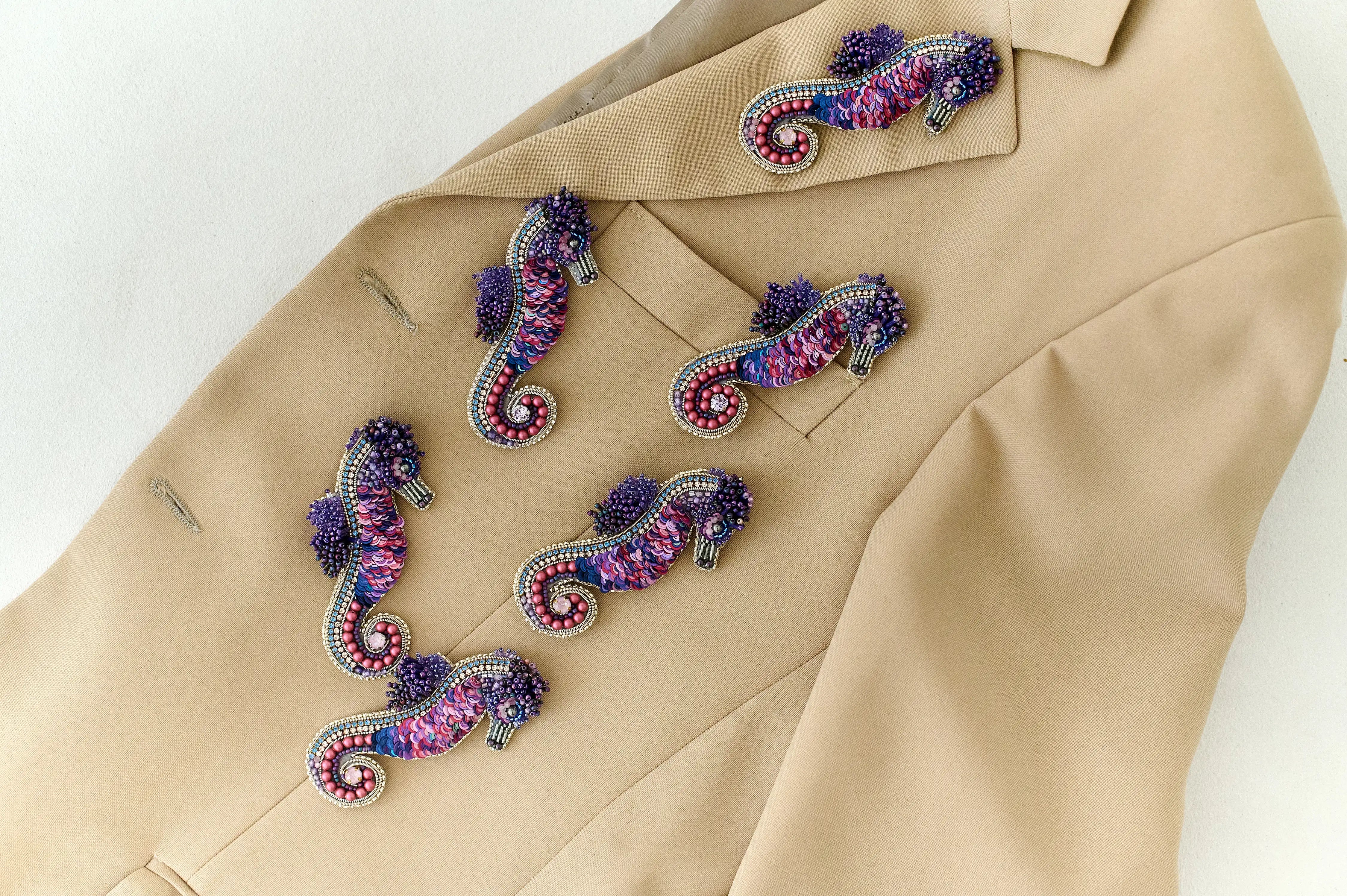 Colorful seahorse-shaped brooches on a beige jacket