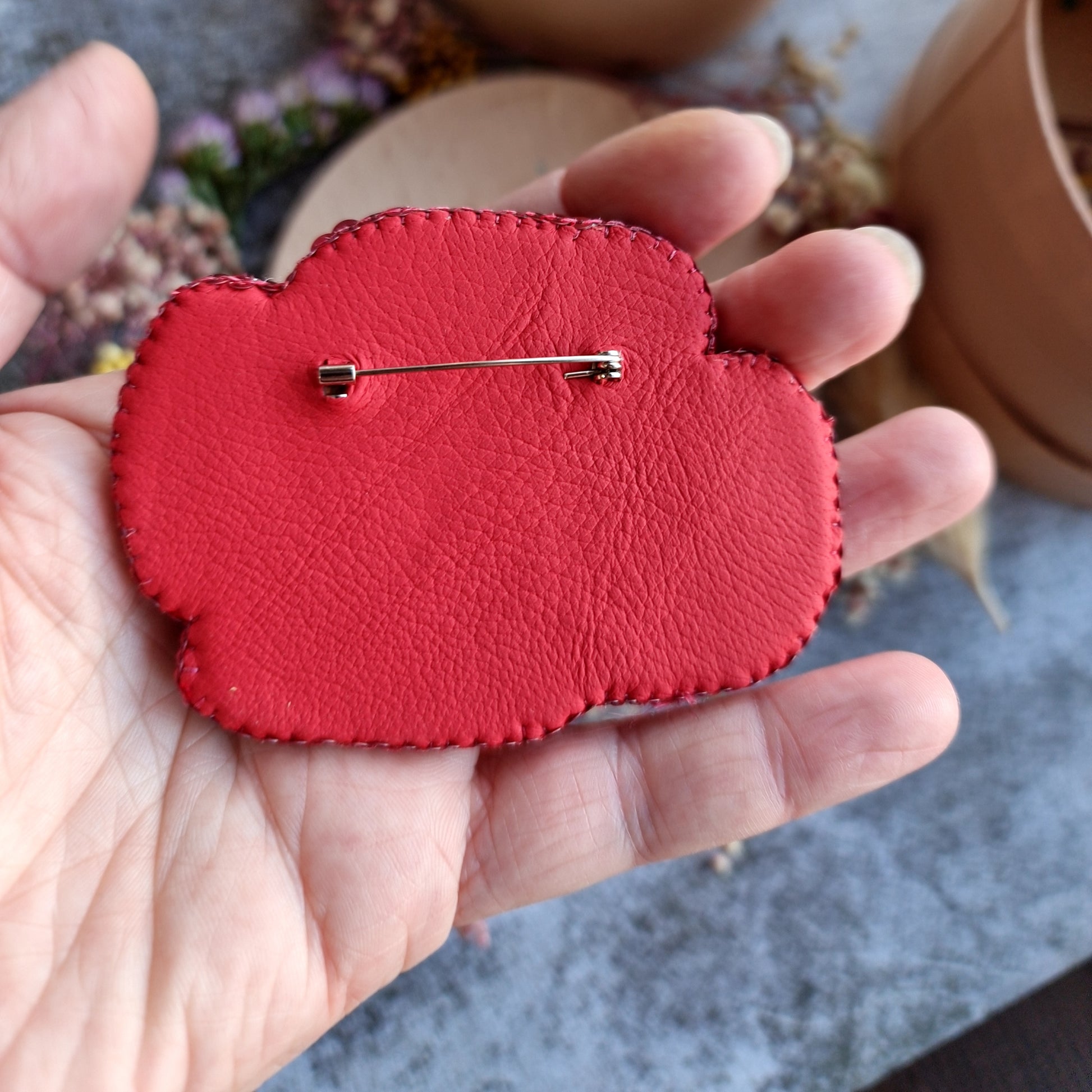 Red heart-shaped object with a pin held in a hand against a blurred outdoor background