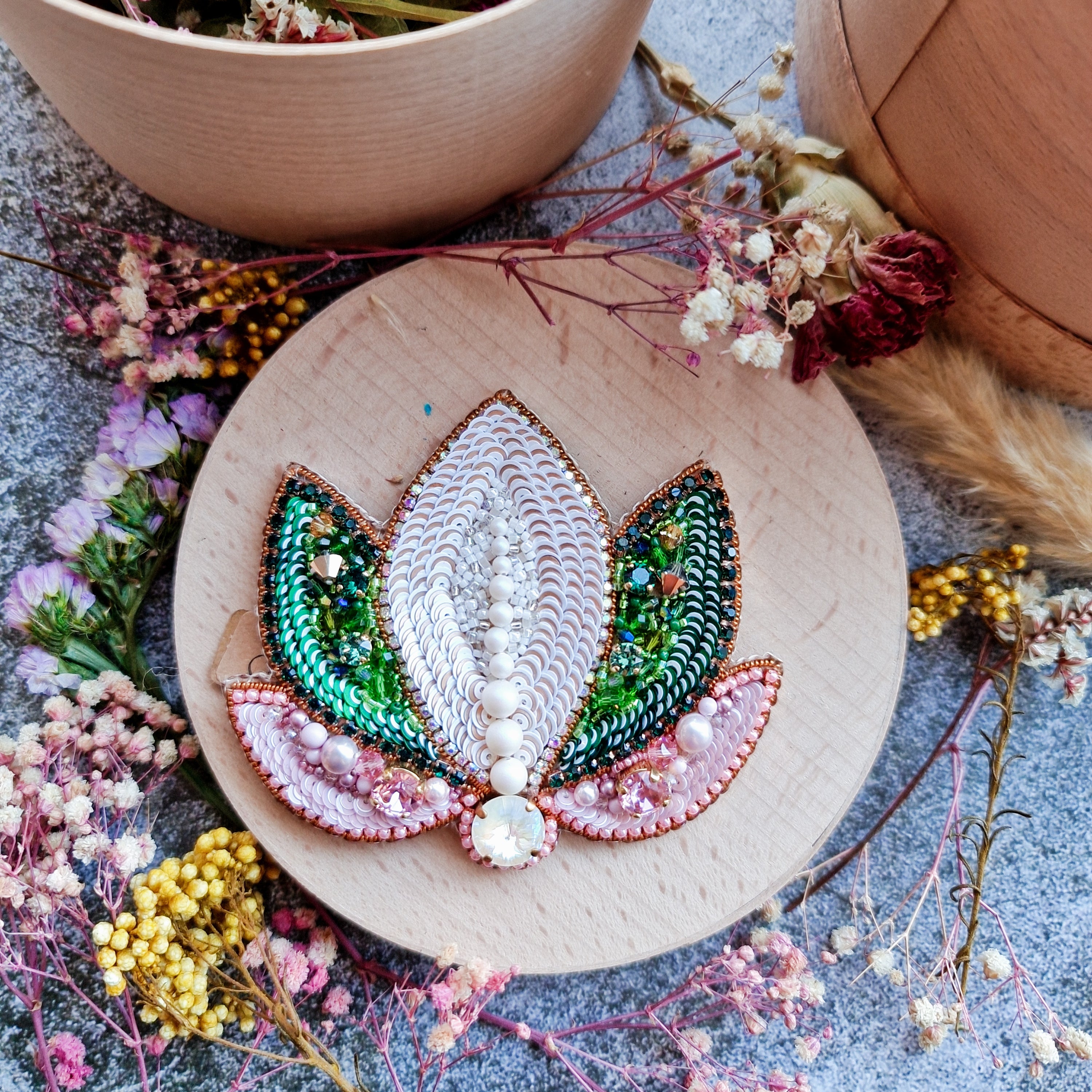Decorative embroidery hoop with a leaf design surrounded by dried flowers on a textured surface