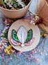 Decorative embroidery hoop with a leaf design surrounded by dried flowers on a textured surface