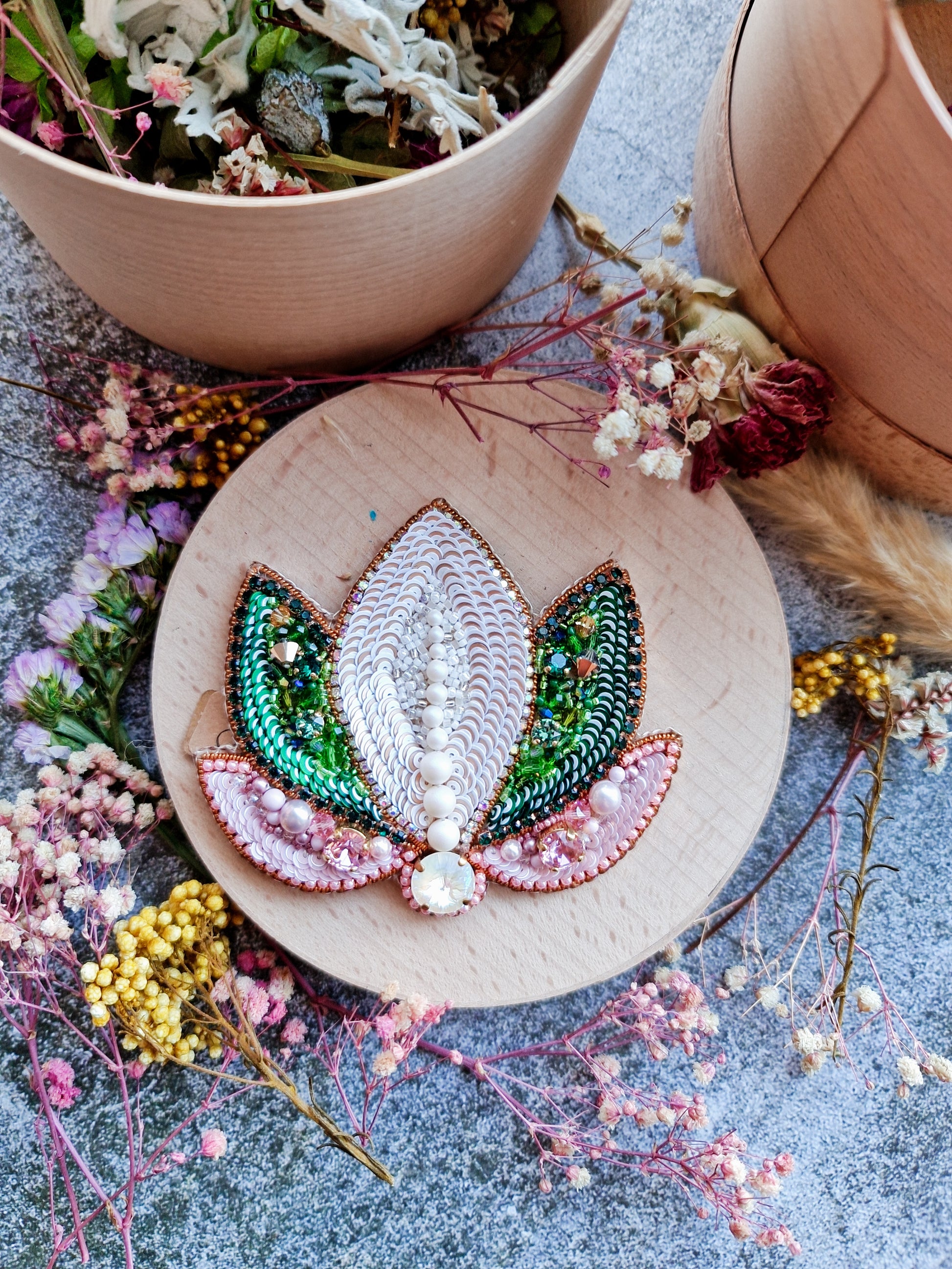 Decorative embroidery hoop with a leaf design surrounded by dried flowers on a textured surface