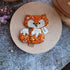 Handmade fox beaded brooch in orange tones with fluffy white tail detail and embroidered face