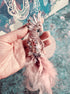 Decorative fish ornament with pink feathers held by a hand on a textured surface.