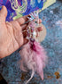 Decorative keychain with pink feathers held by a hand on a textured surface.