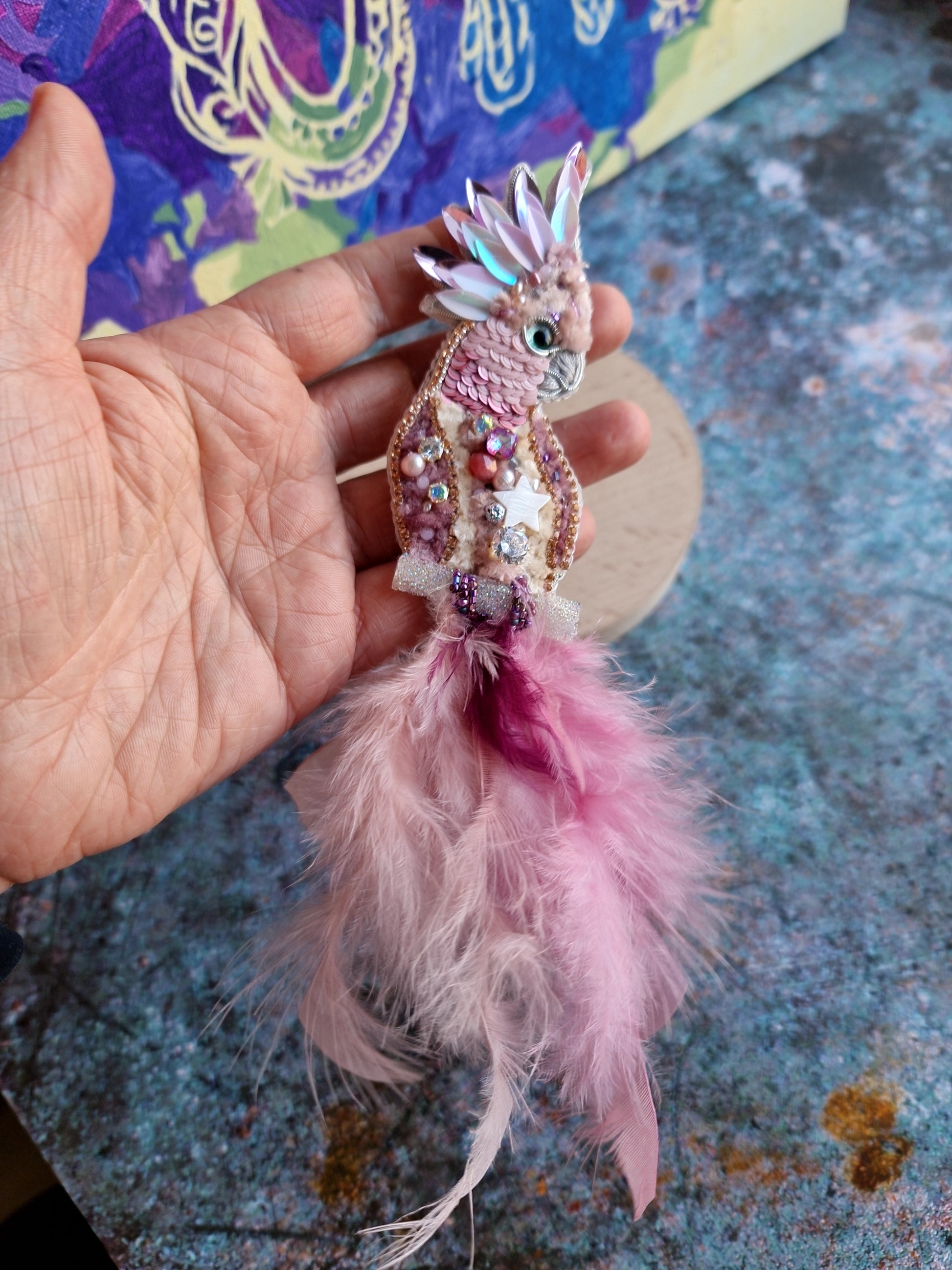 Decorative keychain with pink feathers held by a hand on a textured surface.