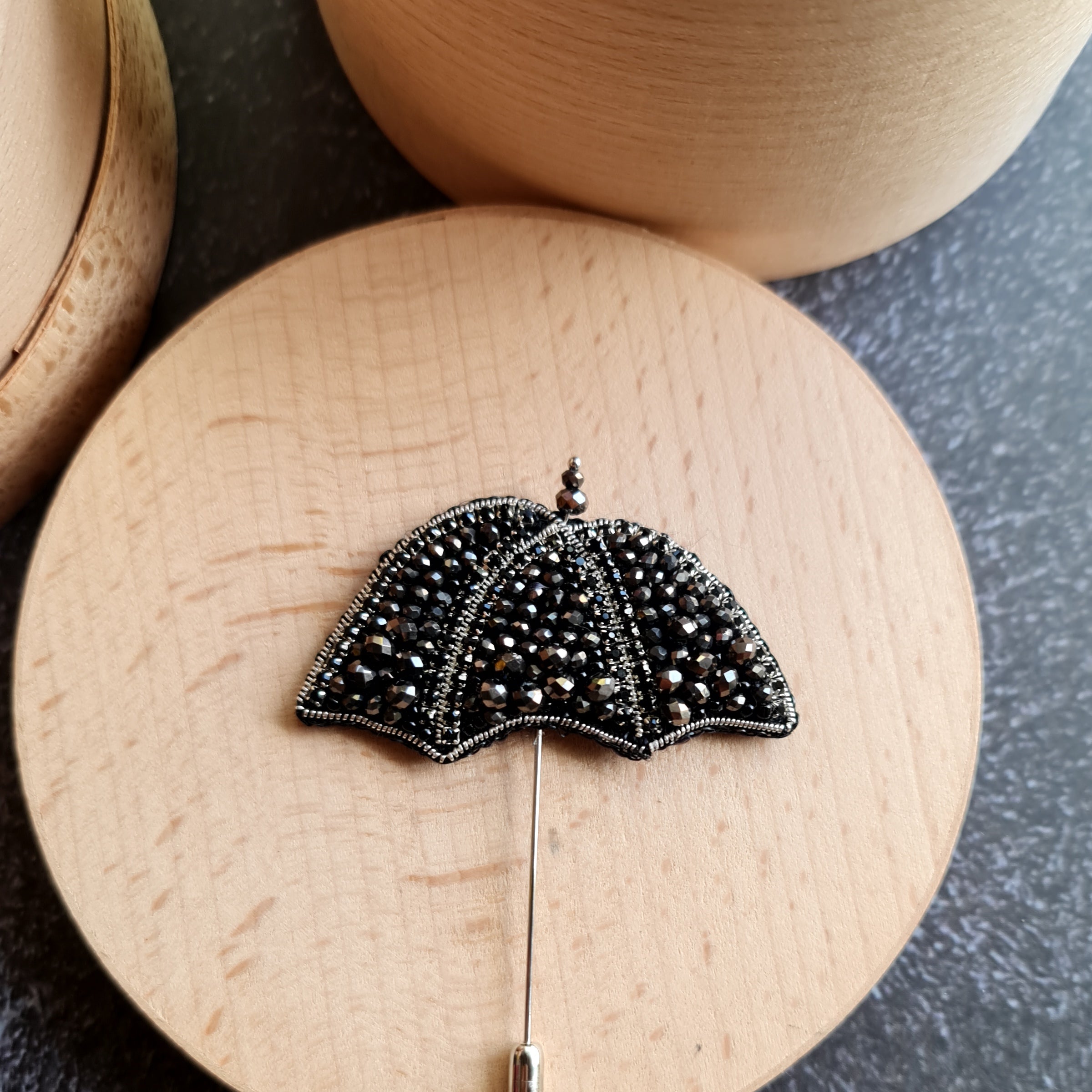 Black beaded umbrella brooch on a wooden surface with a dark background