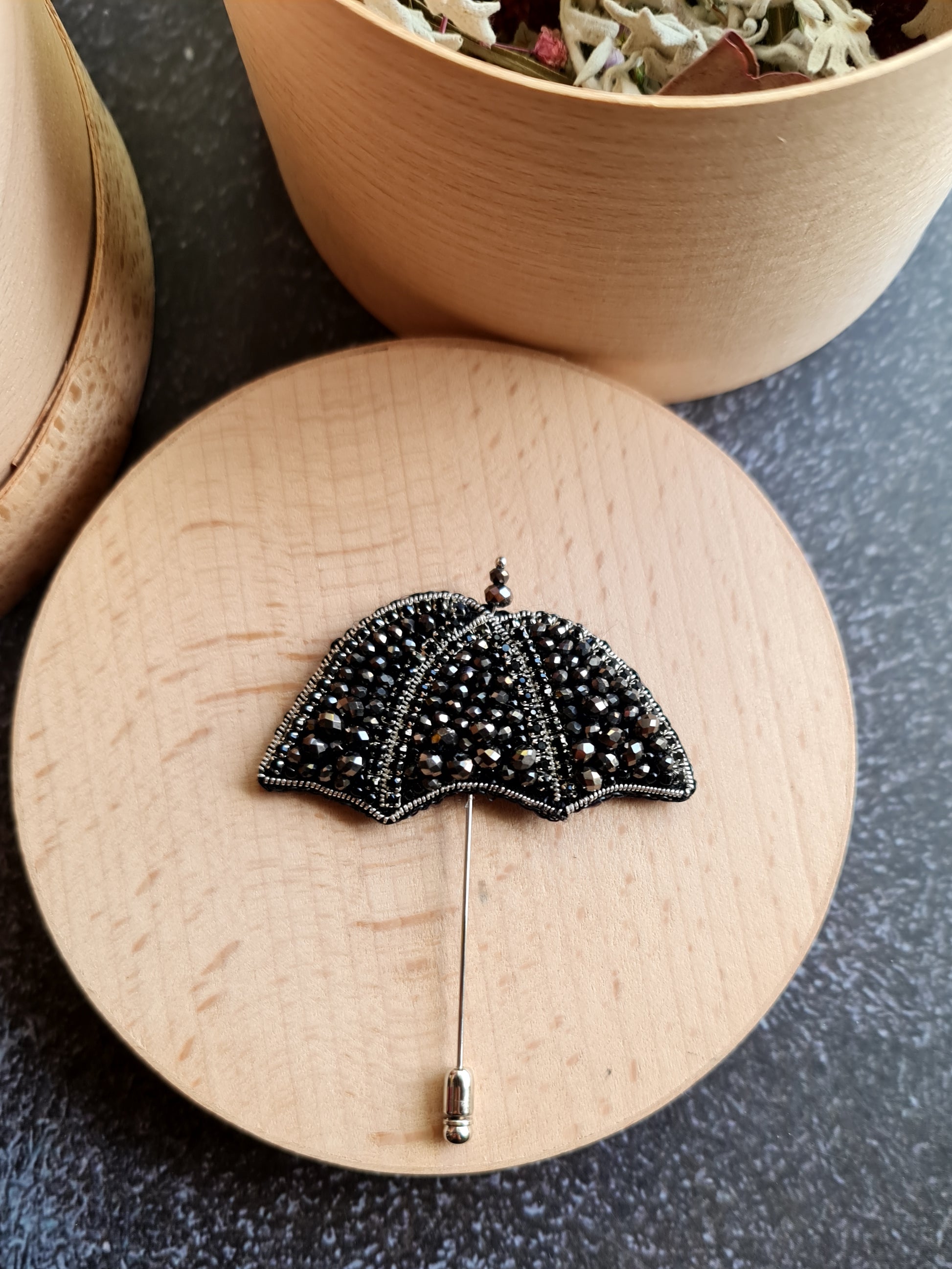 Black beaded umbrella brooch on a wooden surface with a dark background