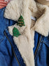 Blue denim jacket with white fur lining and green Christmas tree pins.