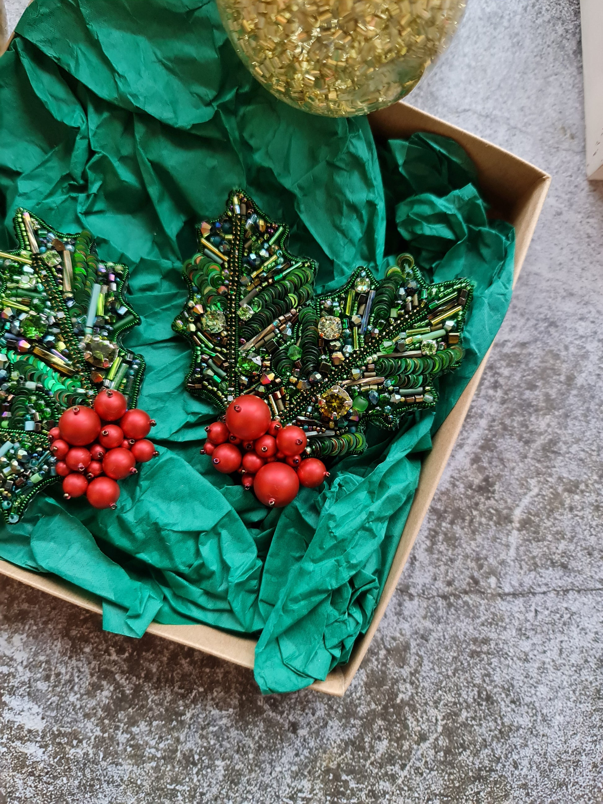 Decorative Christmas tree made of green beads and red ornaments in a box on a textured surface.