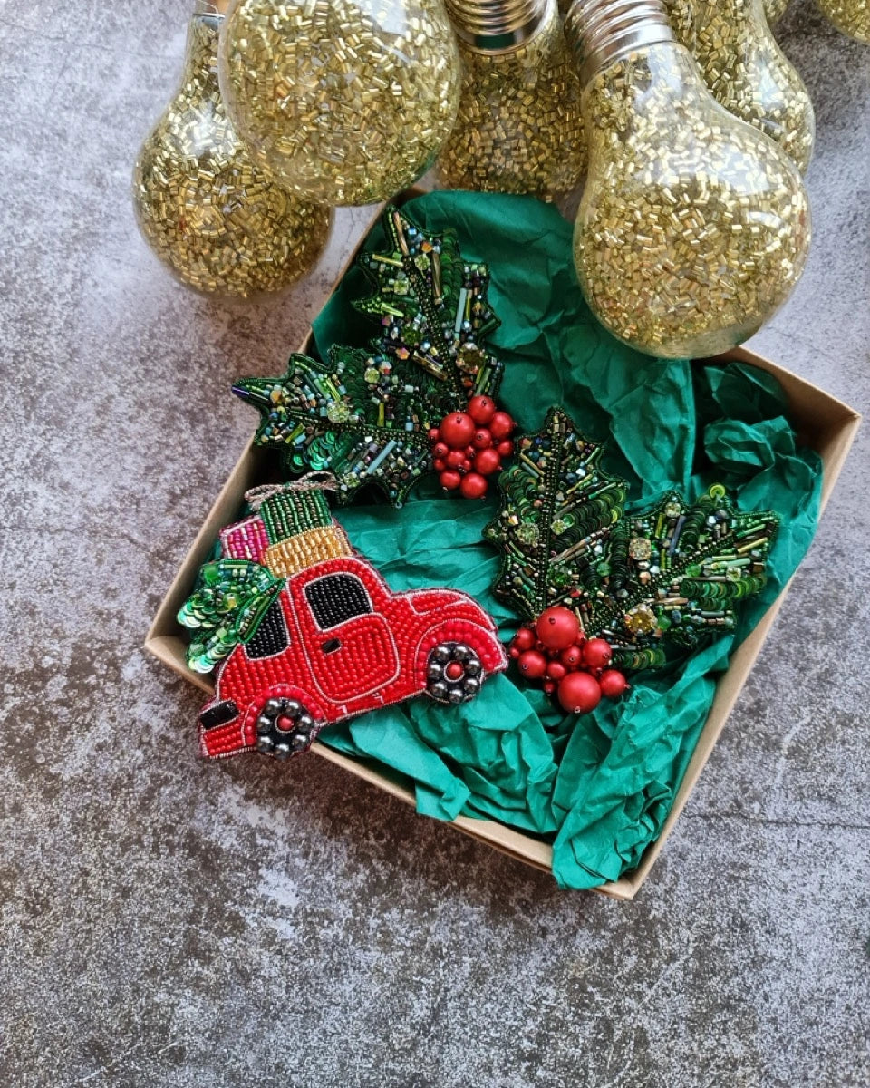 Decorative box with a red truck ornament, greenery, and glittery lights on a gray surface.