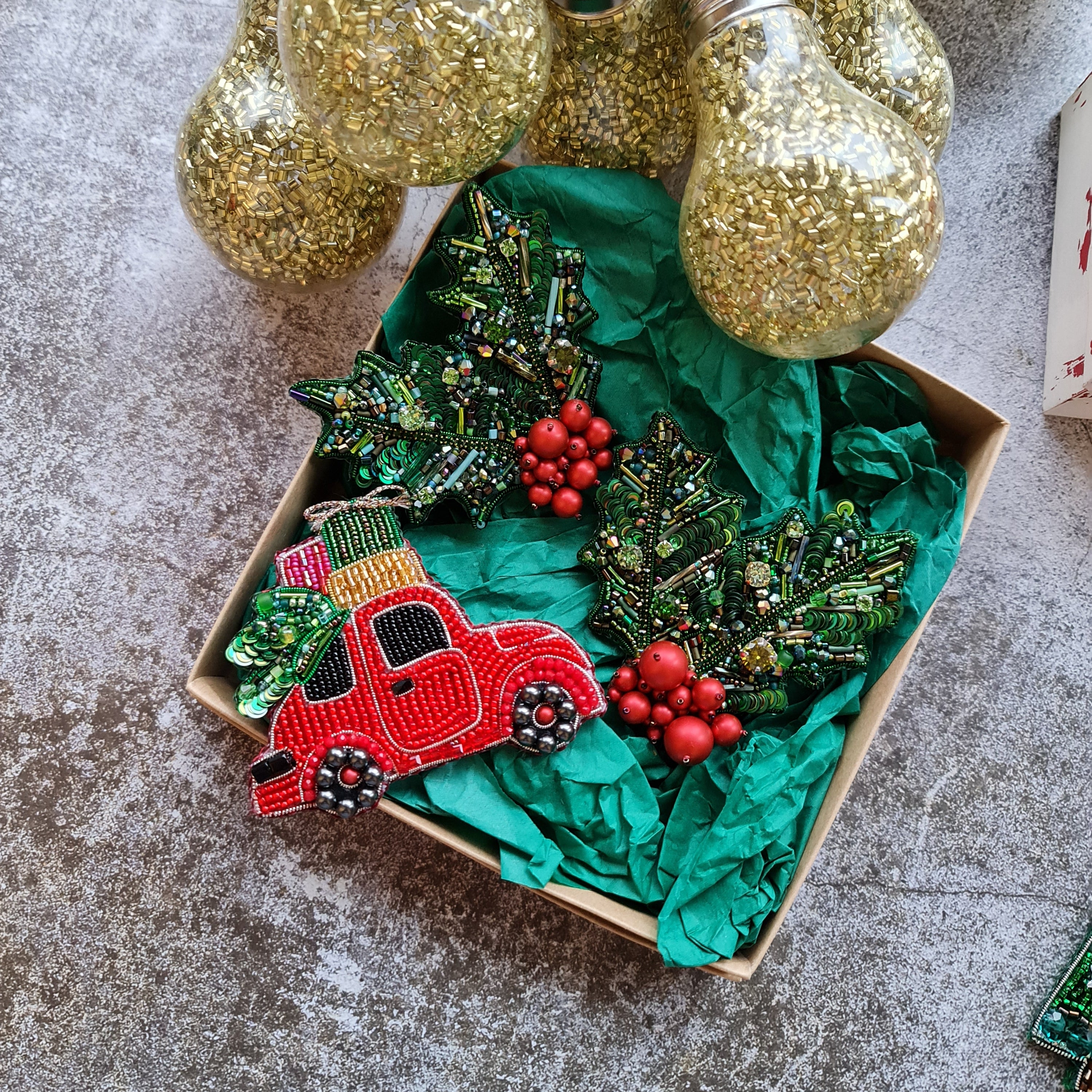 Decorative Christmas wreath with red car and holly berries in a box, surrounded by gold light bulbs on a textured surface.