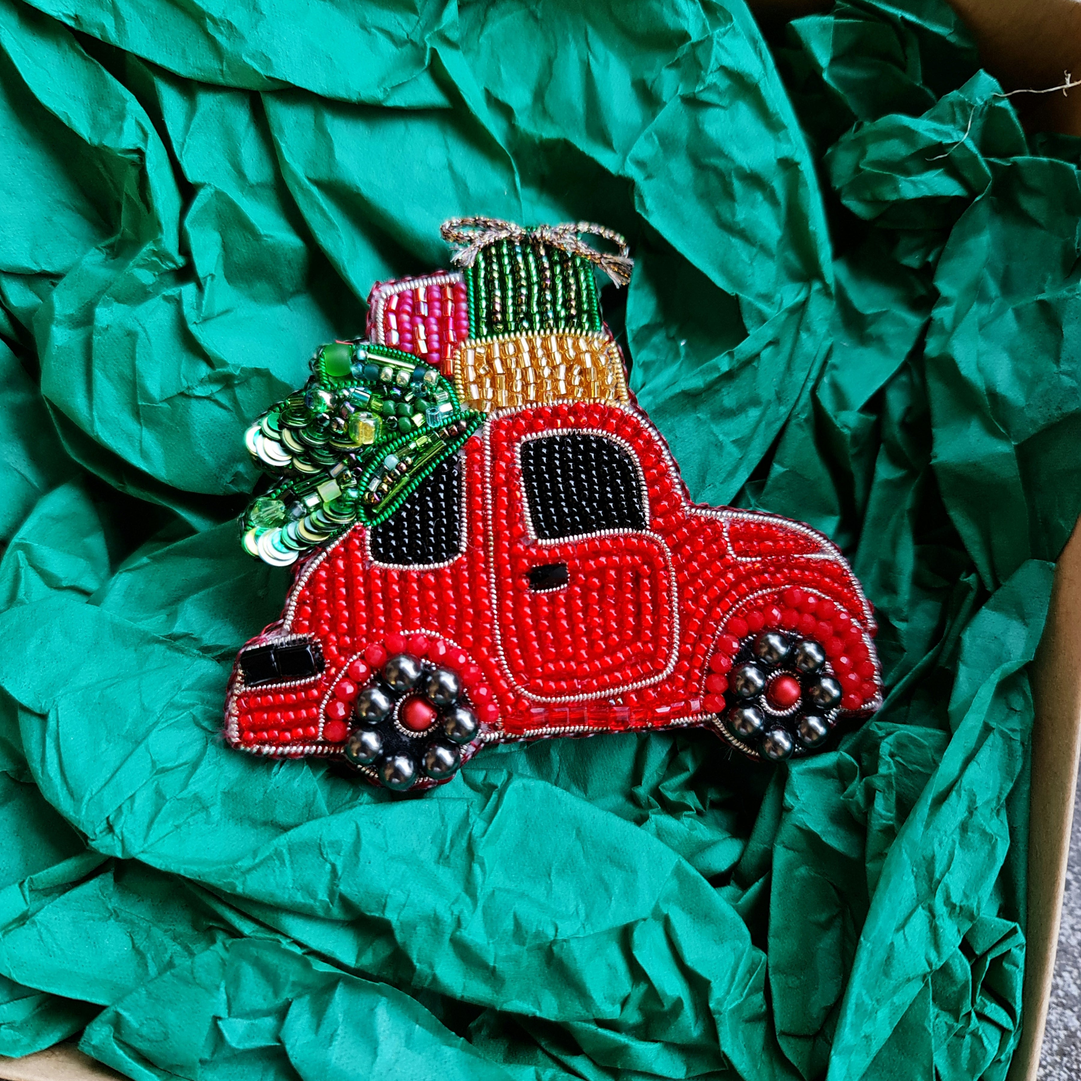 Decorative red truck ornament with green tree on top, wrapped in green tissue paper.