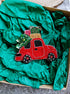 Decorative red truck ornament with green tree on top, wrapped in green tissue paper.