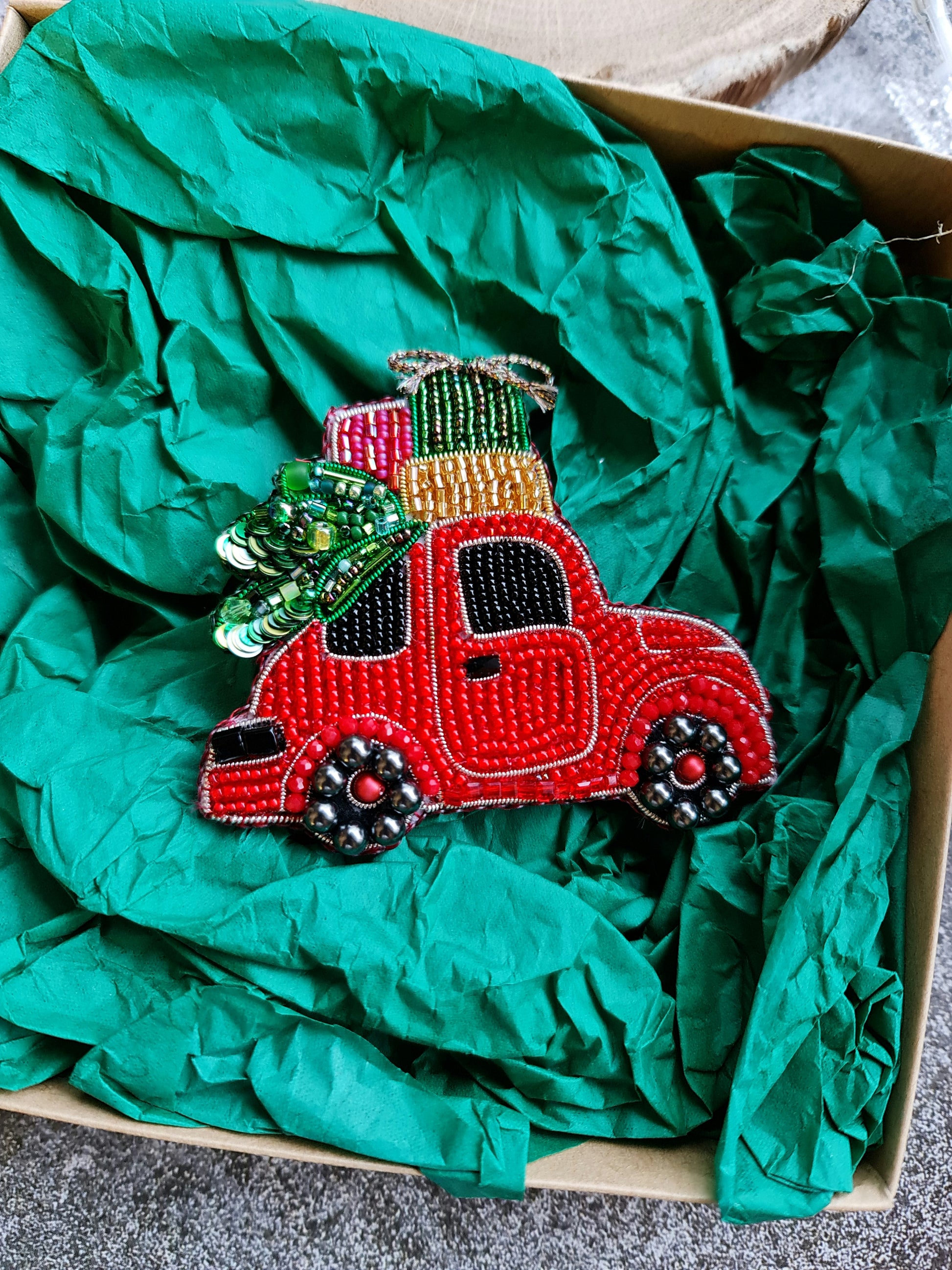 Decorative red truck ornament with green tree on top, wrapped in green tissue paper.