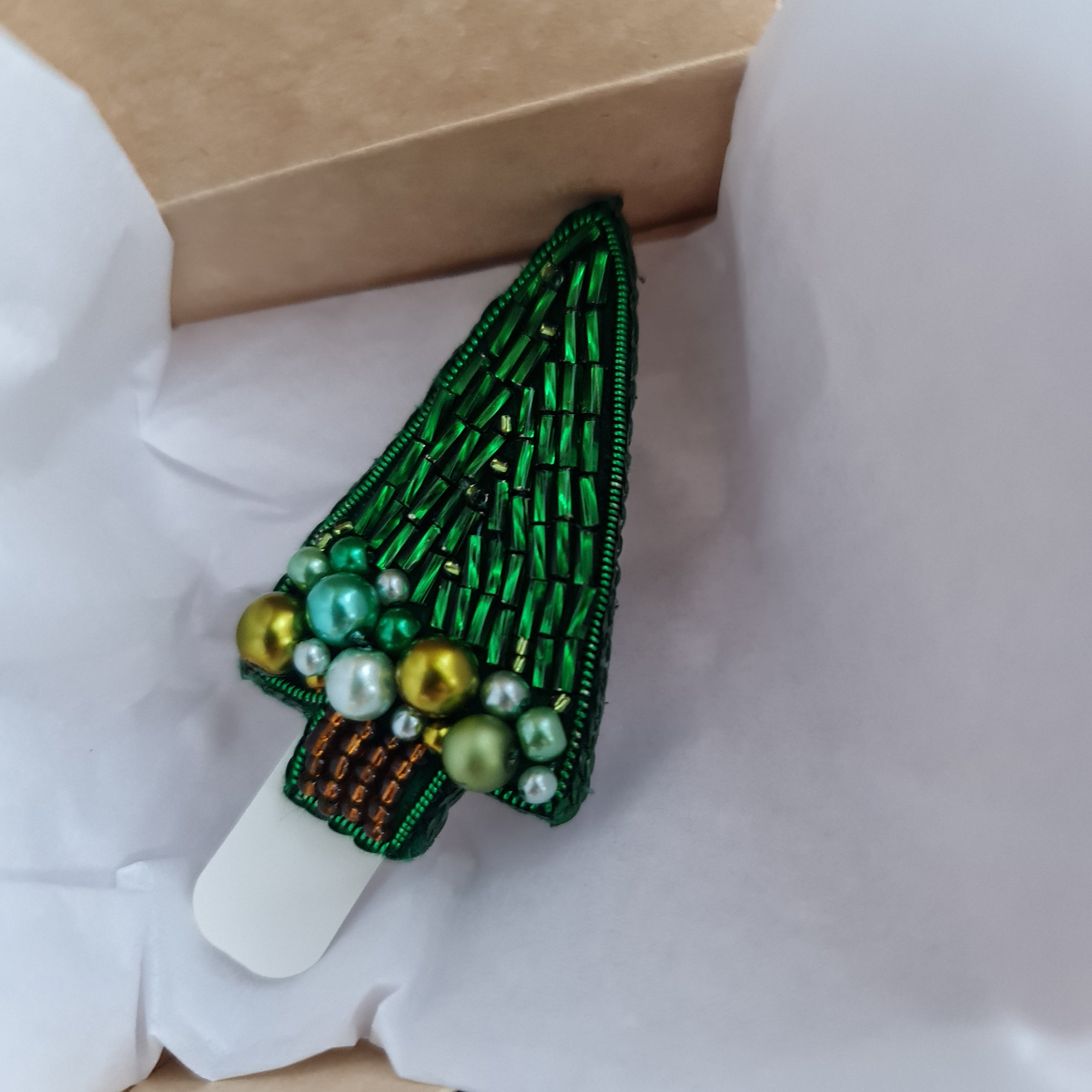 Green beaded brooch on a white shirt with a cardboard box in the background