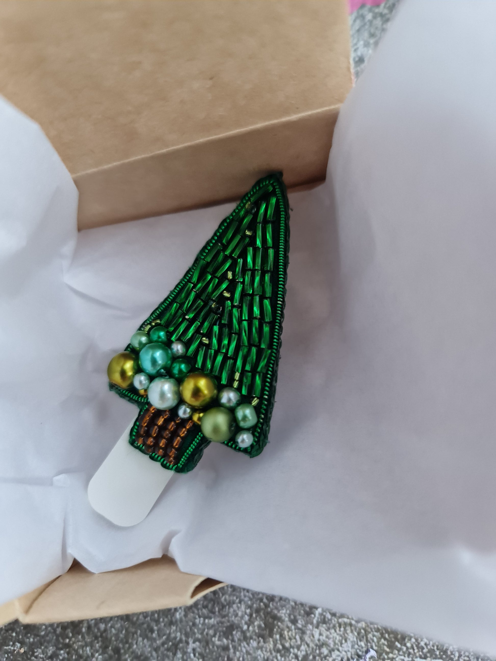 Green beaded brooch on a white shirt with a cardboard box in the background