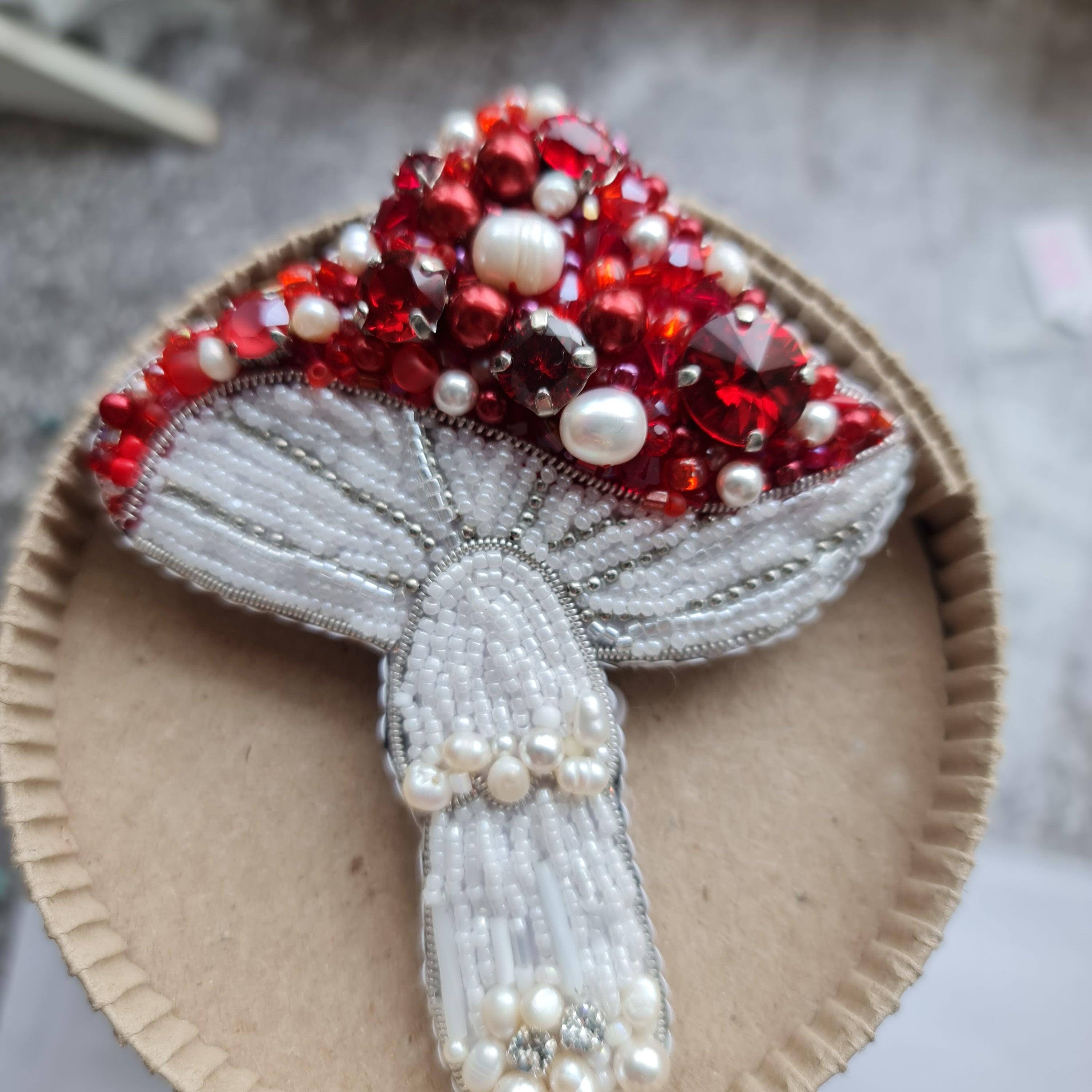 Red beaded mushroom brooch embroidered with ruby crystals, pearls and white beadwork on dark fabric background