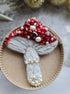 Red beaded mushroom brooch embroidered with ruby crystals, pearls and white beadwork on dark fabric background