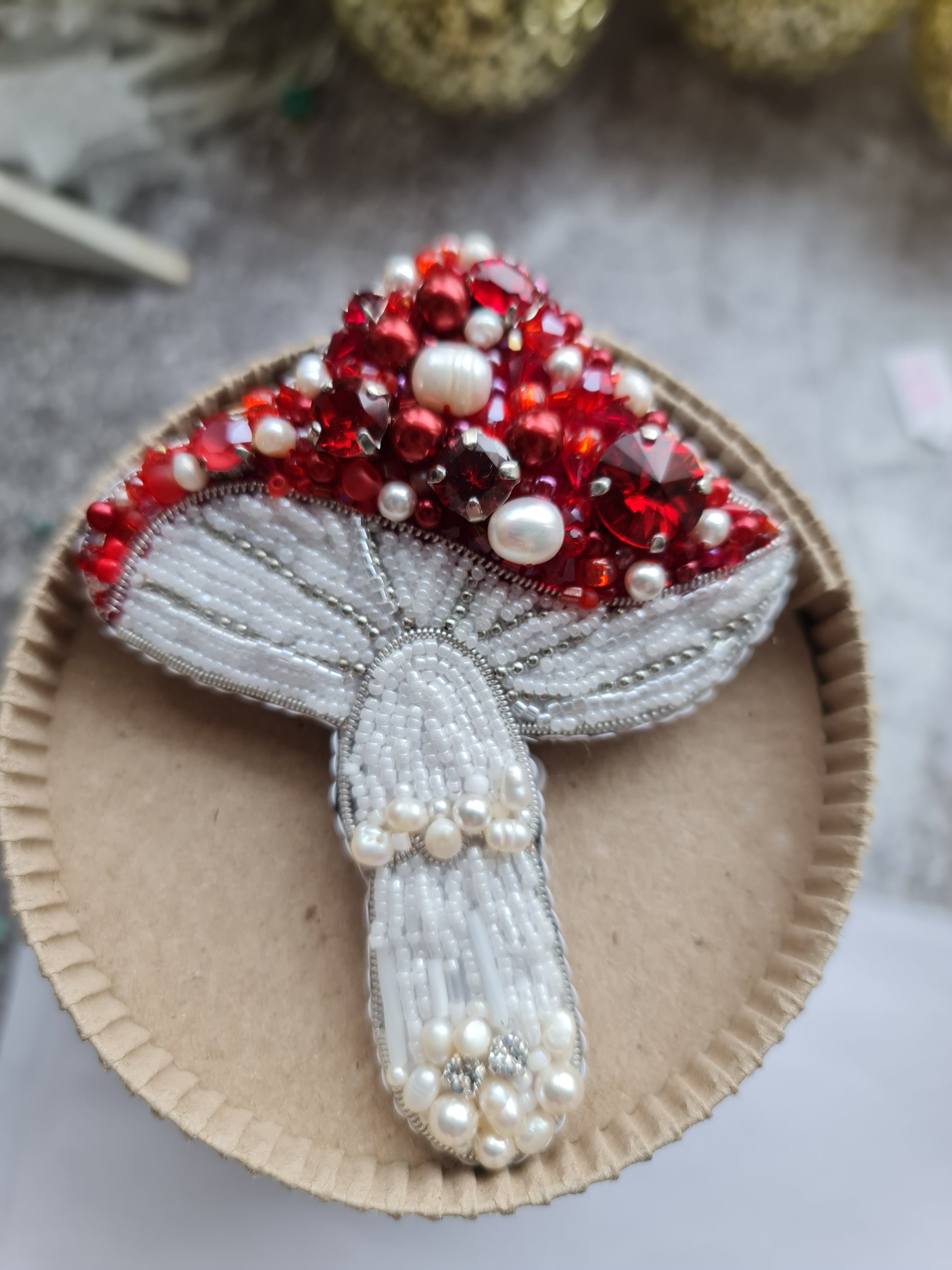 Red beaded mushroom brooch embroidered with ruby crystals, pearls and white beadwork on dark fabric background