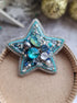 Star-shaped decorative item with blue and silver embellishments on a cardboard surface.