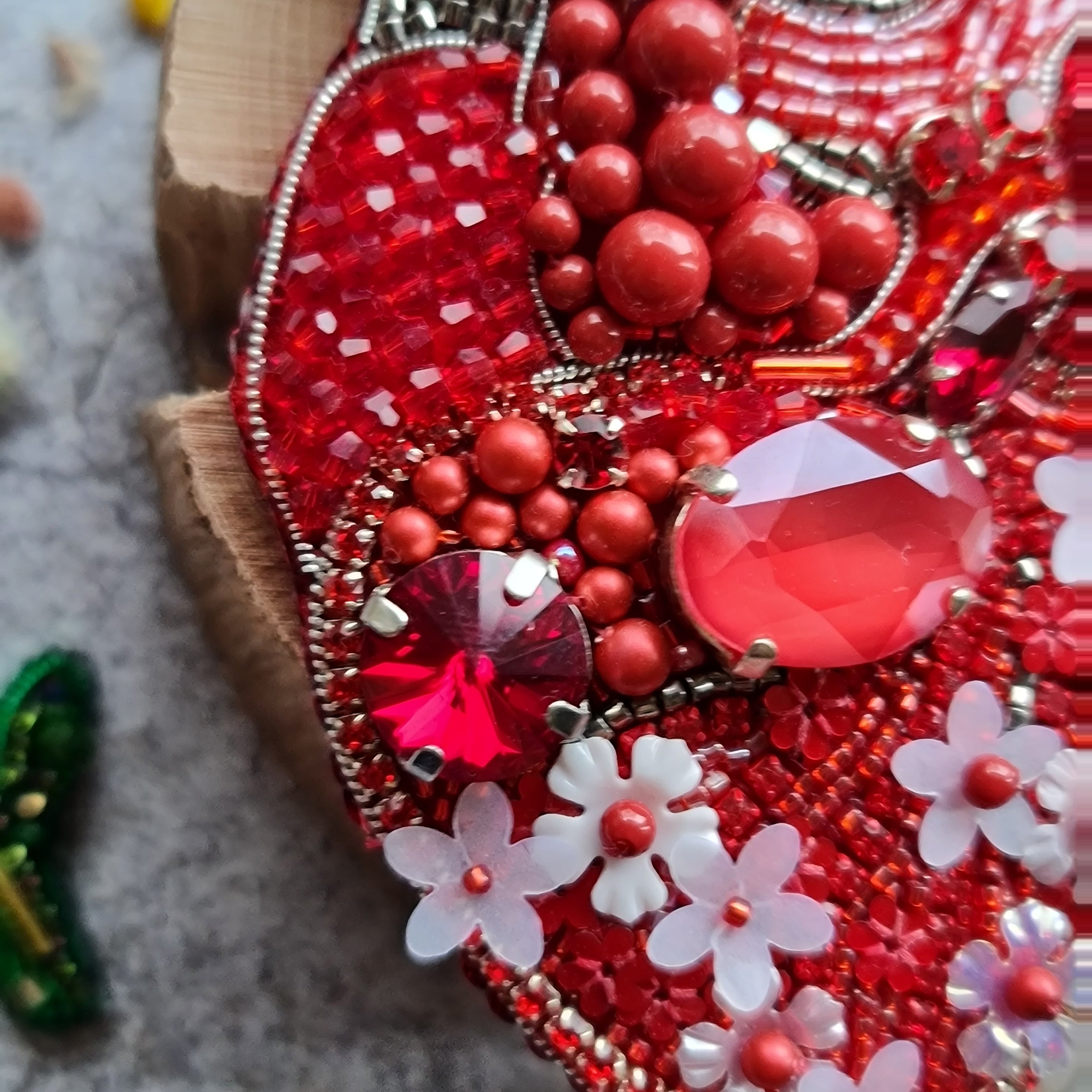 Decorative item with red beads, flowers, and gemstones on a textured surface