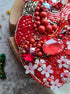 Decorative item with red beads, flowers, and gemstones on a textured surface
