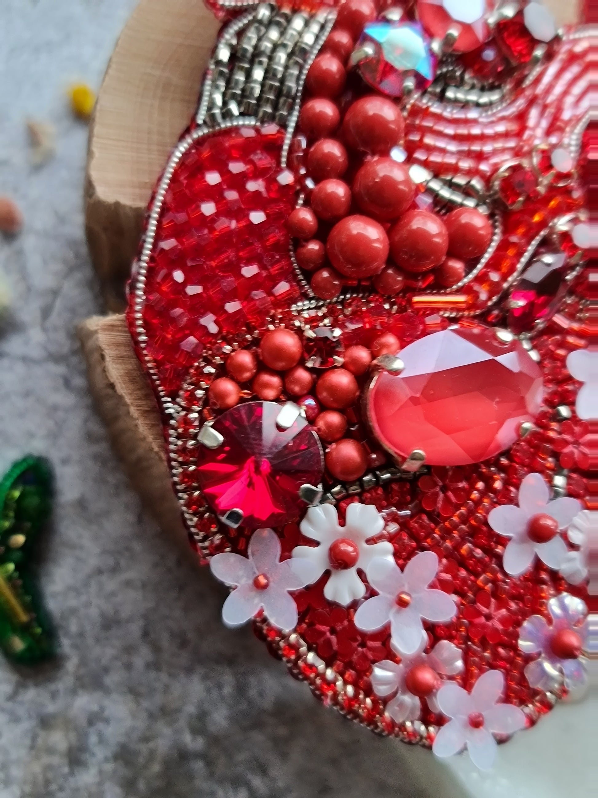 Decorative item with red beads, flowers, and gemstones on a textured surface