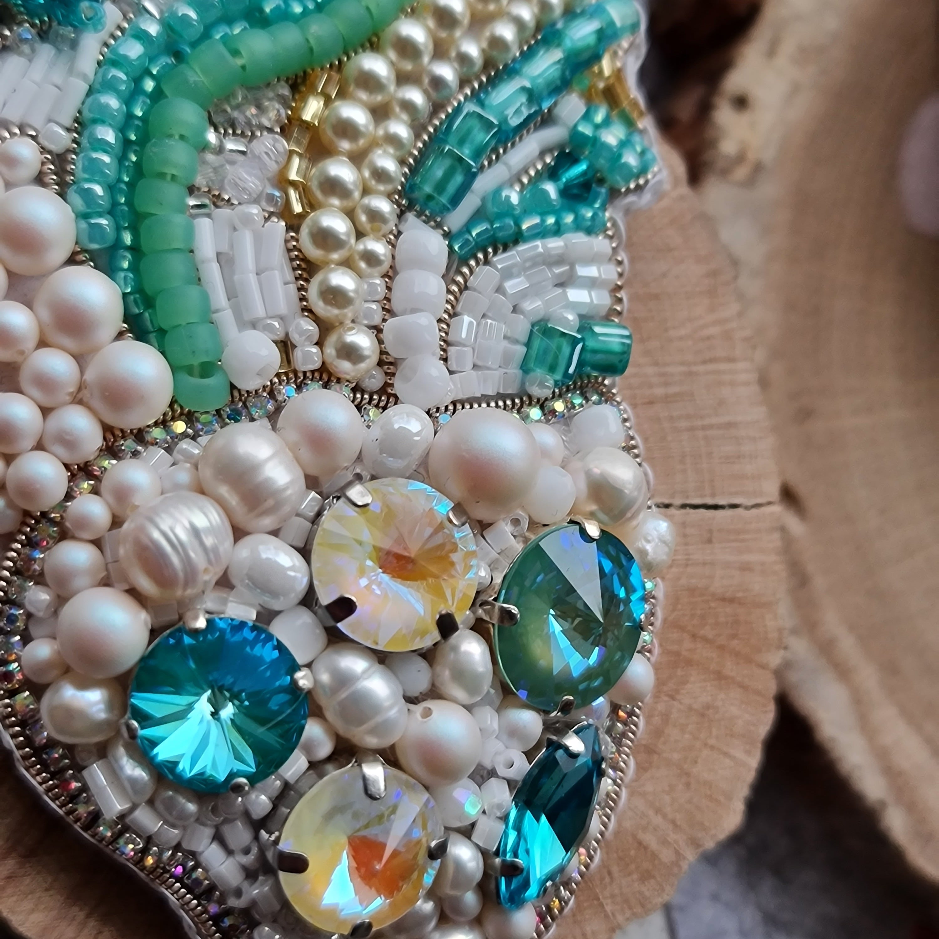 Decorative brooch with pearls, beads, and gemstones on a wooden surface