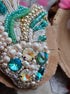 Decorative brooch with pearls, beads, and gemstones on a wooden surface