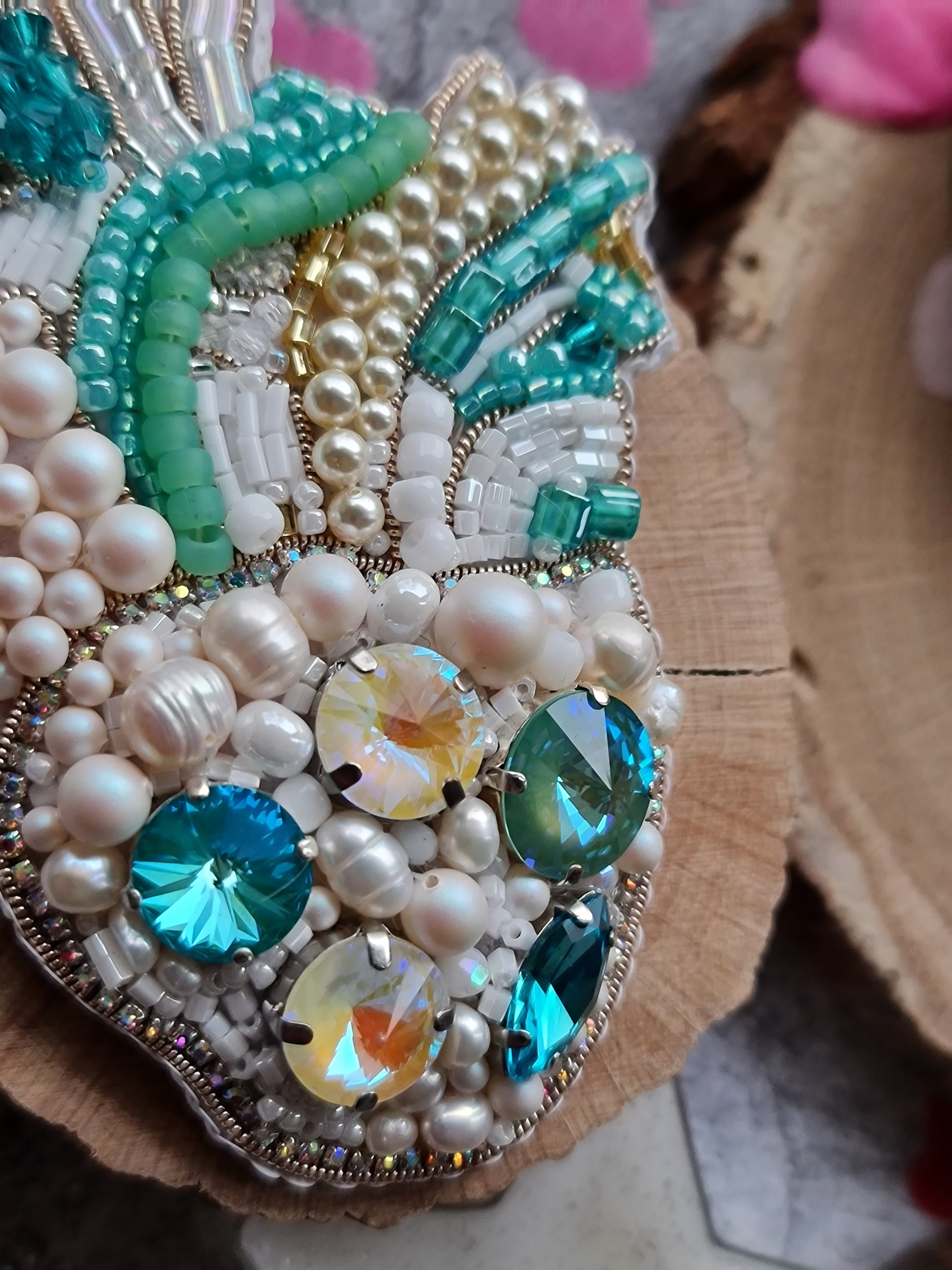 Decorative brooch with pearls, beads, and gemstones on a wooden surface