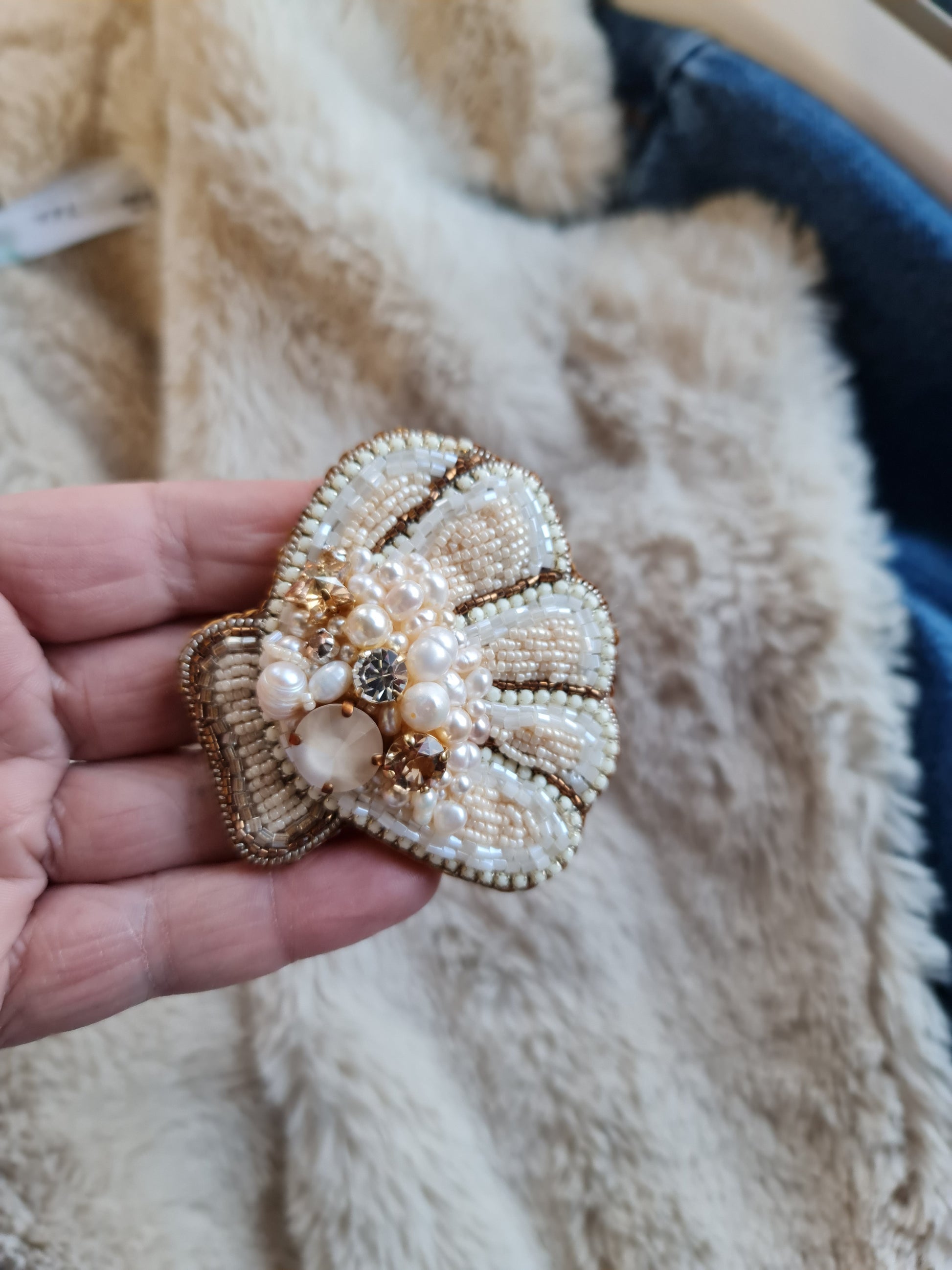 Hand holding a decorative shell brooch with pearls and gold details on a textured surface.