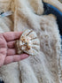 Decorative shell brooch with pearls and gold accents held in a hand against a textured beige background.