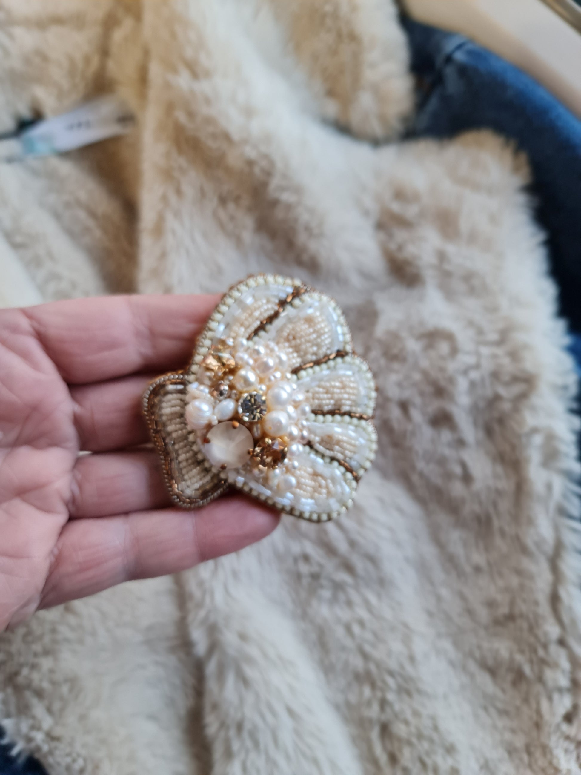 Decorative shell brooch with pearls and gold accents held in a hand against a textured beige background.