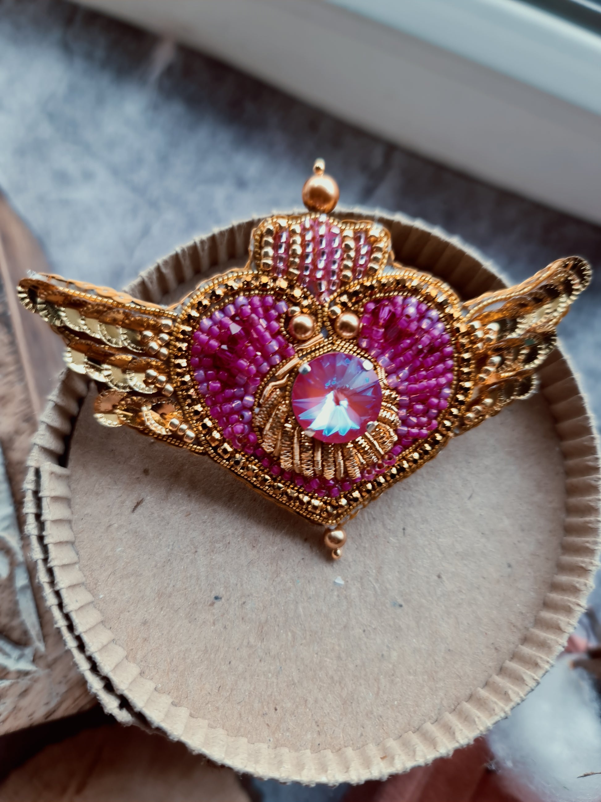 Close-up of a handmade Cosmic Heart Compact Brooch showing detailed beadwork and embroidered patterns on a celestial heart motif.