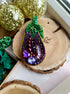 Decorative eggplant-shaped ornament with gemstones on a wooden surface