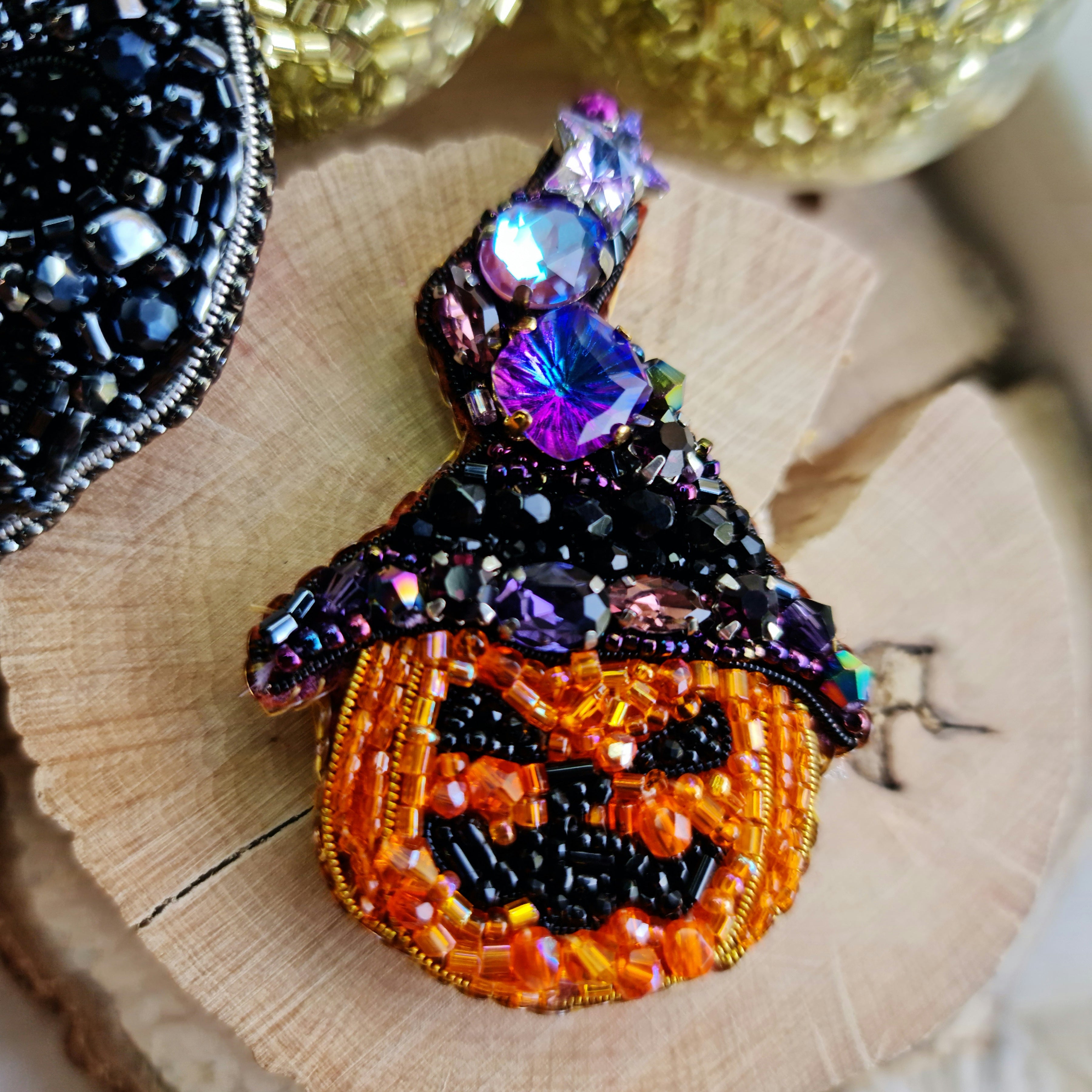 Decorative brooch shaped like a jack-o'-lantern with beaded details on a wooden surface.