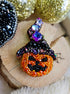 Decorative brooch shaped like a jack-o'-lantern with beaded details on a wooden surface.