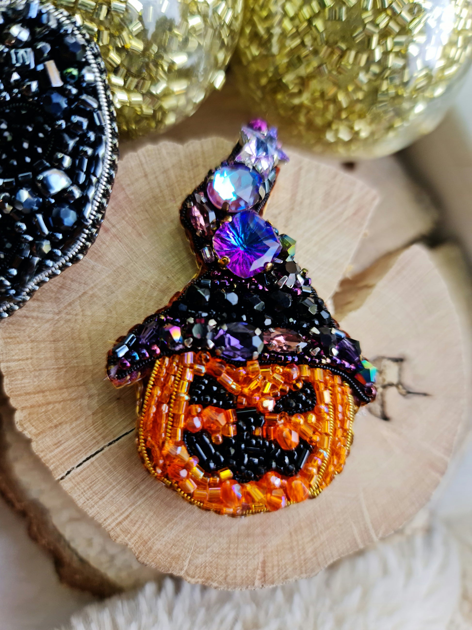Decorative brooch shaped like a jack-o'-lantern with beaded details on a wooden surface.