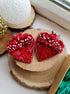 A pair of red heart-shaped beaded earrings with rhinestone accents, displayed on stacked natural wood slices.