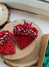 Two red beaded heart-shaped decorative pieces displayed on a round wood slice, with one piece featuring a cluster of faceted red crystals at the top.