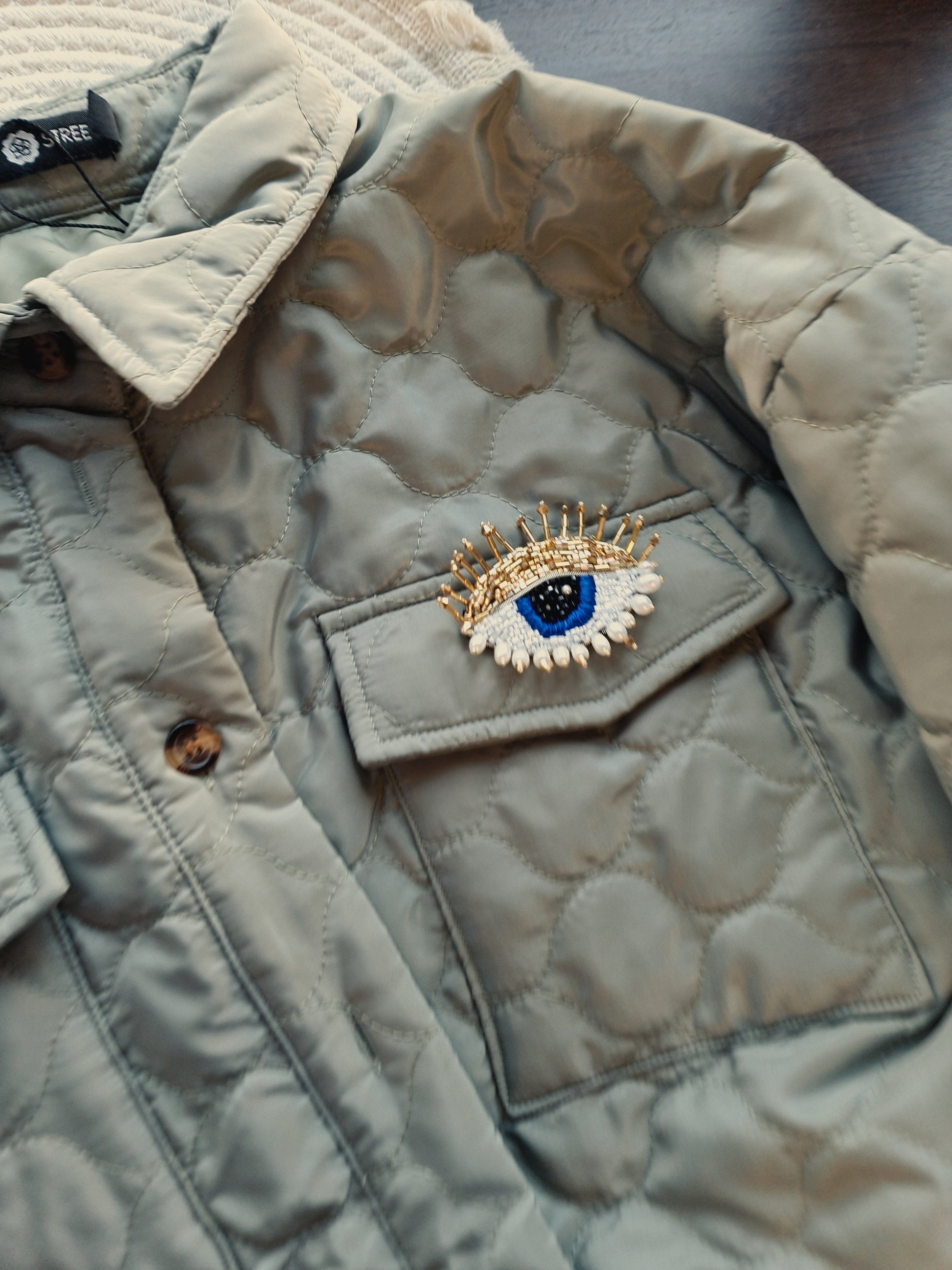 Close-up view of the intricate beadwork on the blue eye brooch, showcasing shimmering glass beads, crystals, and plastic beads fixed onto felt