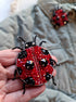 Close-up view of the intricate details on a ladybug brooch, showcasing vibrant embroidery with glass beads, crystals, and plastic beads secured on felt