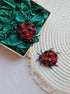 Close-up view of the intricate details on a ladybug brooch, showcasing vibrant embroidery with glass beads, crystals, and plastic beads secured on felt