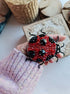 Close-up view of the intricate details on a ladybug brooch, showcasing vibrant embroidery with glass beads, crystals, and plastic beads secured on felt