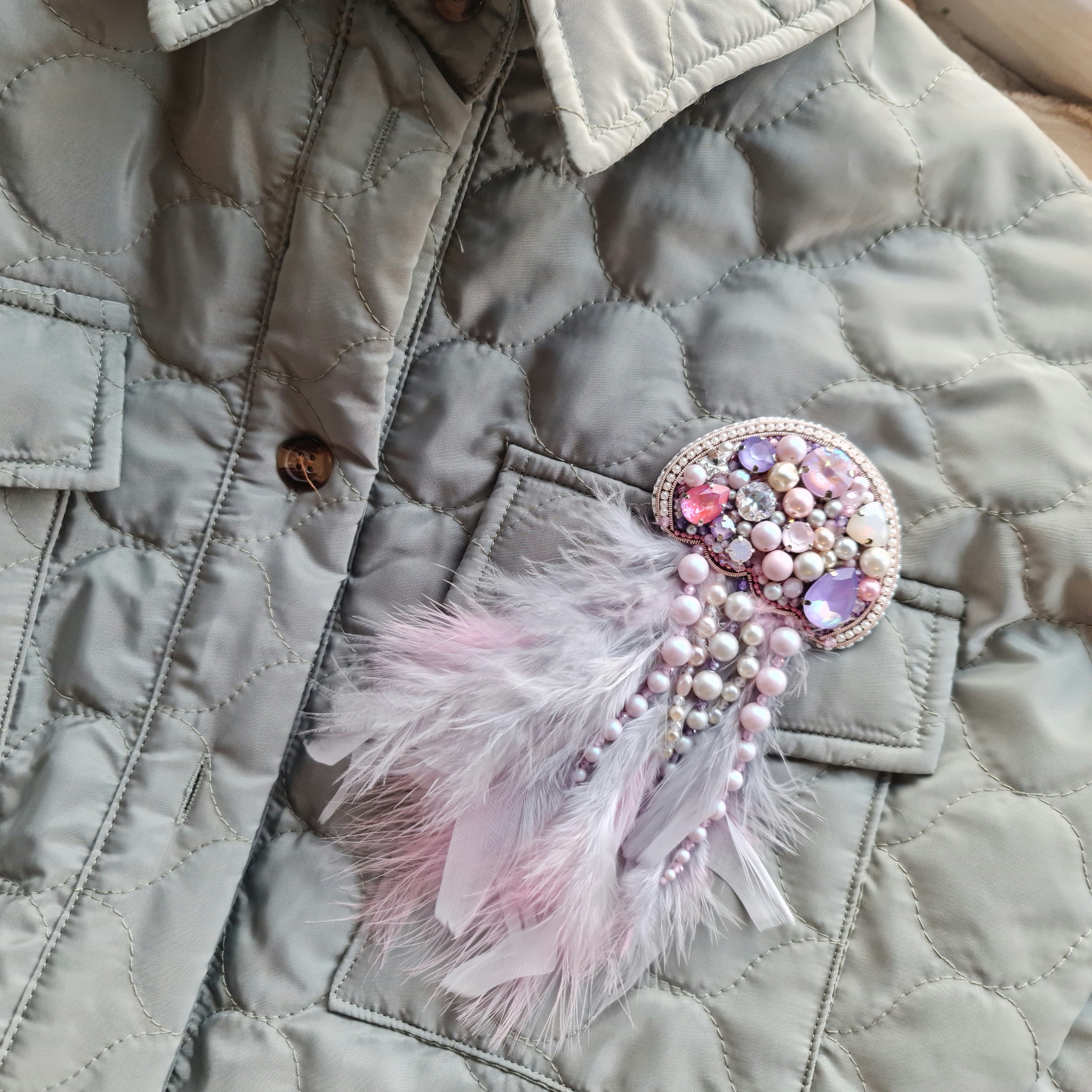 Quilted jacket with a decorative brooch featuring feathers and gemstones.