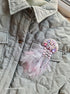 Quilted jacket with a decorative brooch featuring feathers and gemstones.