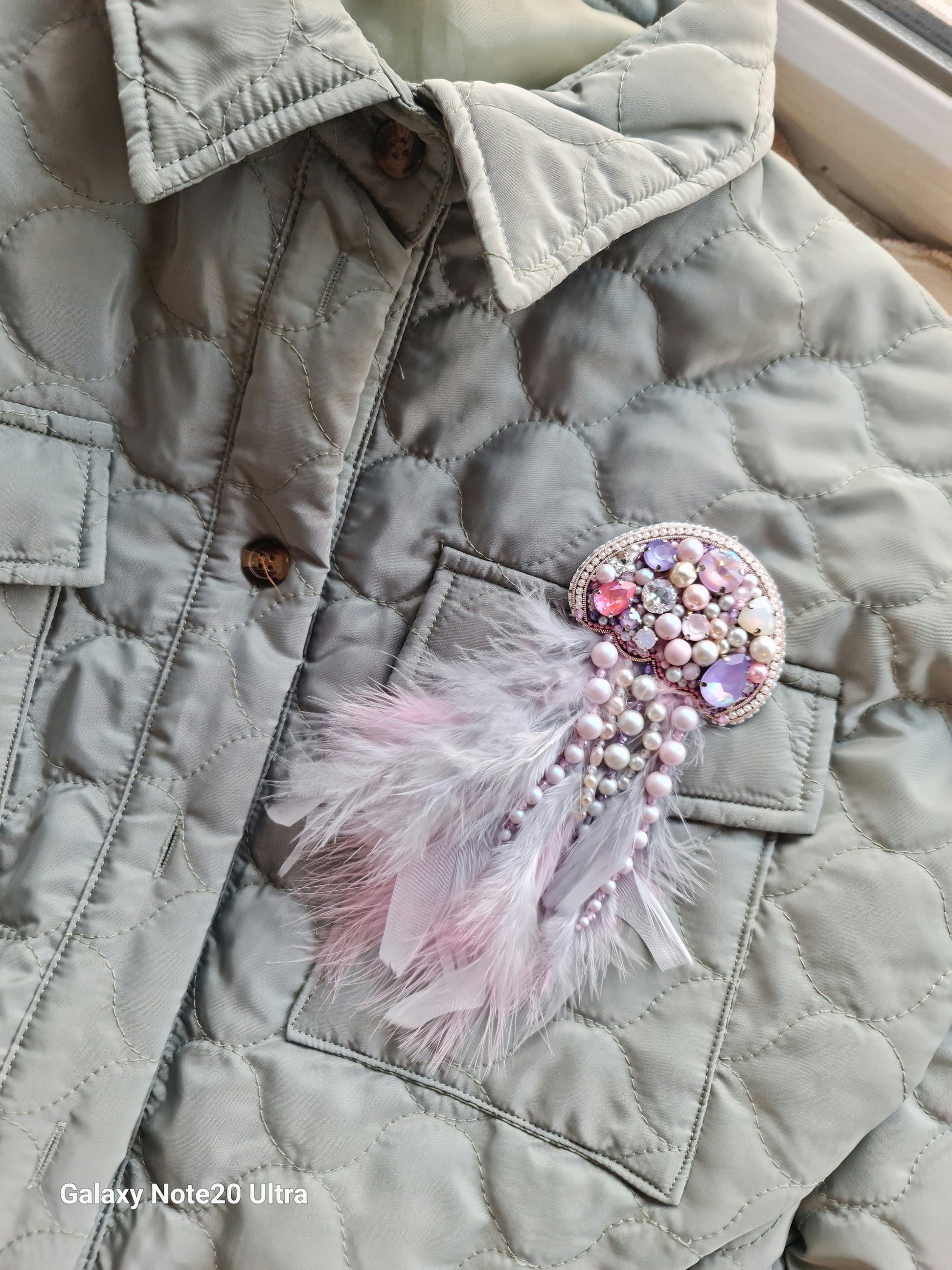 Quilted jacket with a decorative brooch featuring feathers and gemstones.