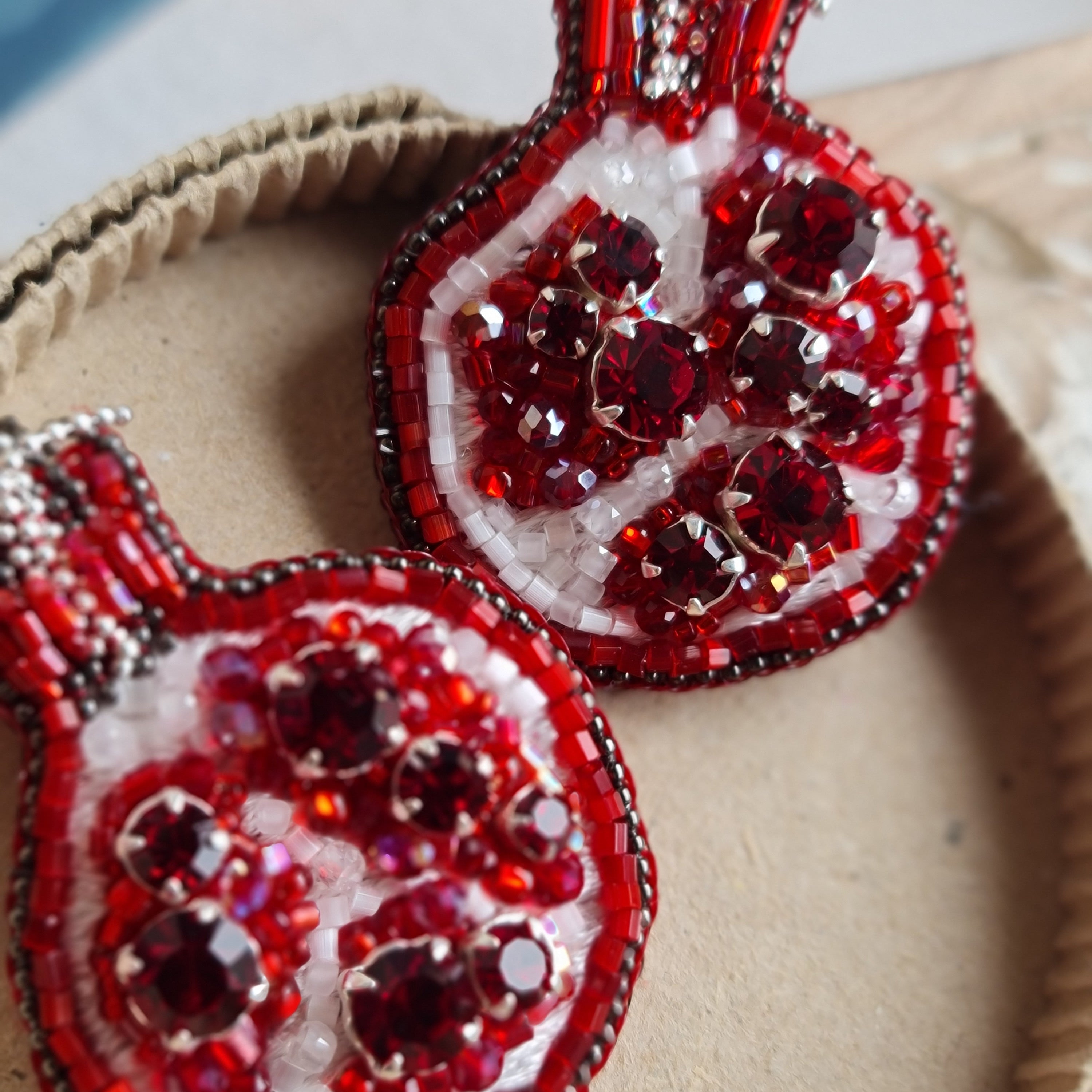 Red beaded pomegranate earrings on a textured surface